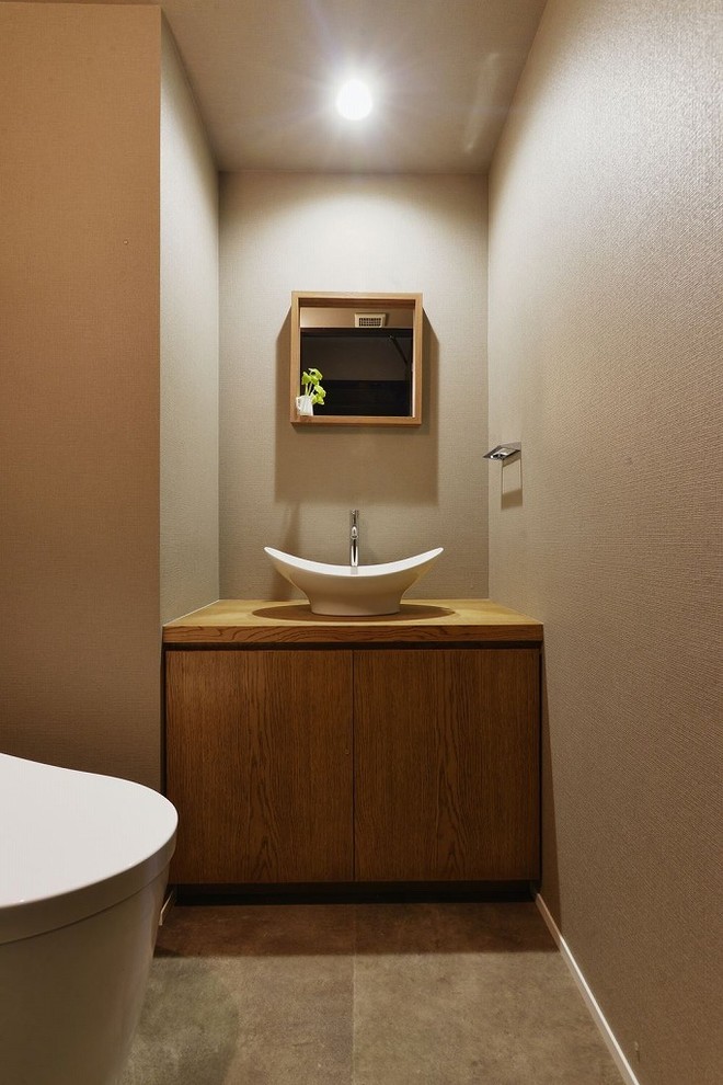This is an example of an asian powder room with flat-panel cabinets, medium wood cabinets, brown walls, a vessel sink, wood benchtops, brown floor and brown benchtops.