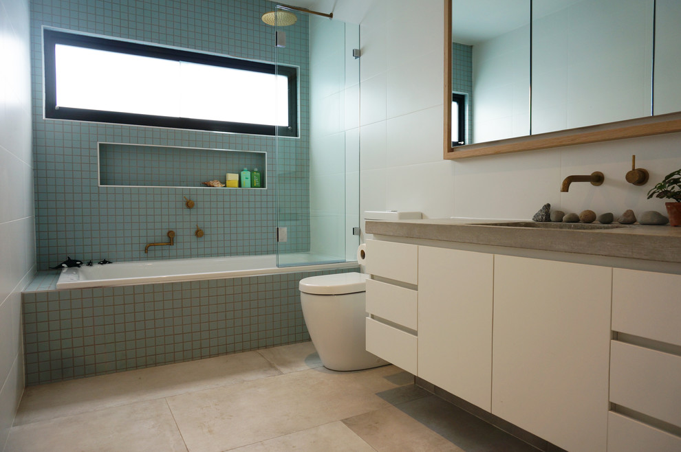 Contemporary kids bathroom in Melbourne with white cabinets, white walls, an undermount sink, concrete benchtops, an alcove tub, a shower/bathtub combo, a two-piece toilet, blue tile and white tile.