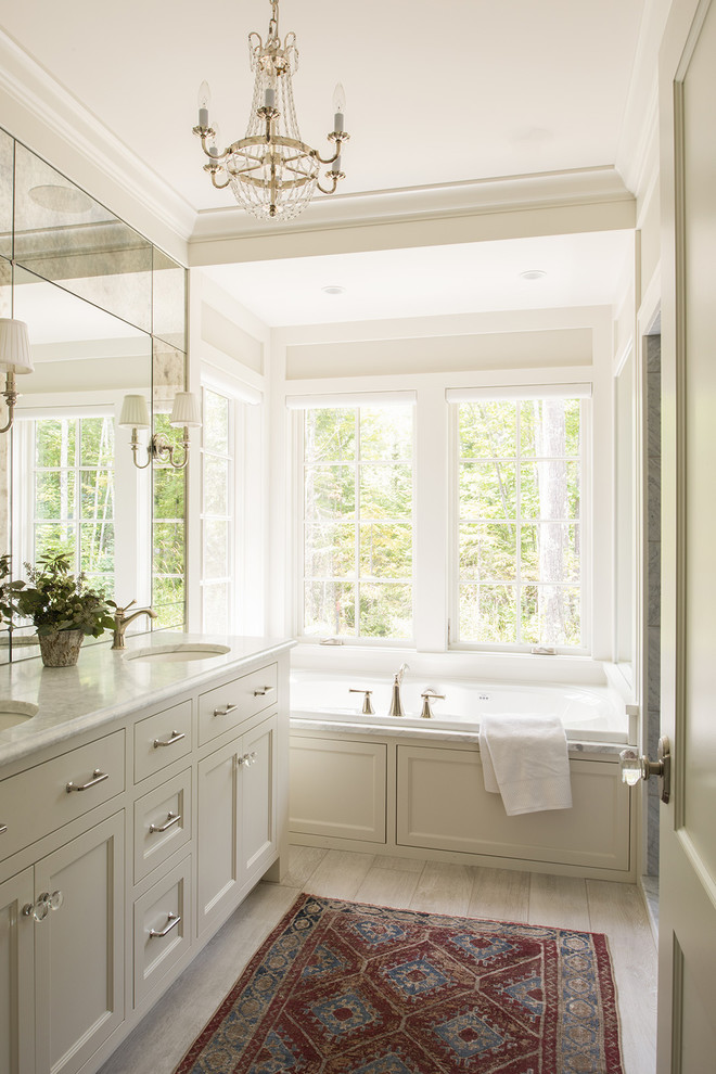 Design ideas for a beach style master bathroom in Minneapolis with shaker cabinets, white cabinets, a drop-in tub, light hardwood floors and an undermount sink.