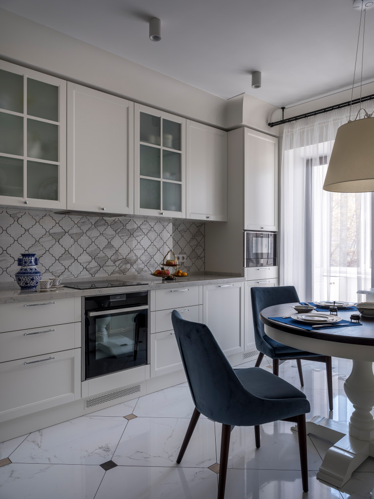 This is an example of a mid-sized transitional l-shaped eat-in kitchen in Moscow with a drop-in sink, raised-panel cabinets, white cabinets, quartz benchtops, grey splashback, porcelain splashback, black appliances, porcelain floors, no island, white floor and grey benchtop.
