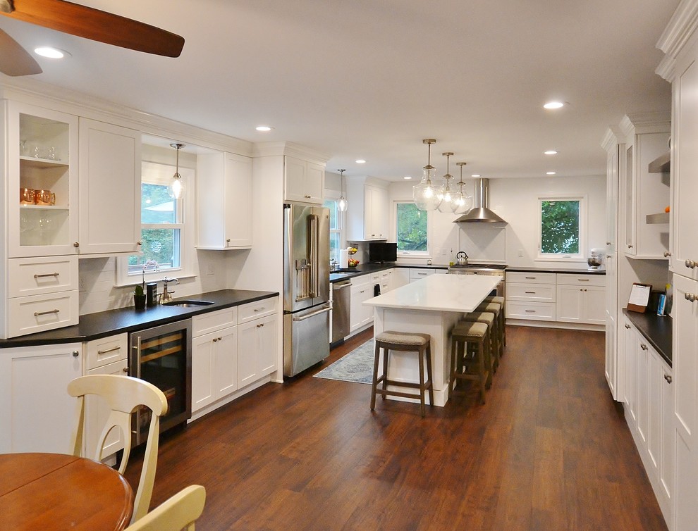 Photo of an expansive transitional u-shaped eat-in kitchen in Philadelphia with an undermount sink, recessed-panel cabinets, white cabinets, quartz benchtops, white splashback, subway tile splashback, stainless steel appliances, vinyl floors, with island, brown floor and white benchtop.
