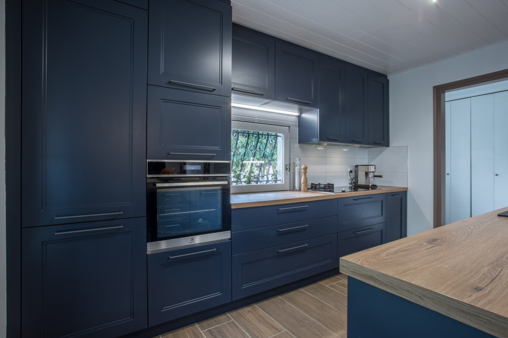 リヨンにある高級な中くらいなカントリー風のおしゃれなキッチン (アンダーカウンターシンク、レイズドパネル扉のキャビネット、青いキャビネット、ラミネートカウンター、白いキッチンパネル、セラミックタイルのキッチンパネル、シルバーの調理設備、セラミックタイルの床、茶色い床、茶色いキッチンカウンター、塗装板張りの天井) の写真