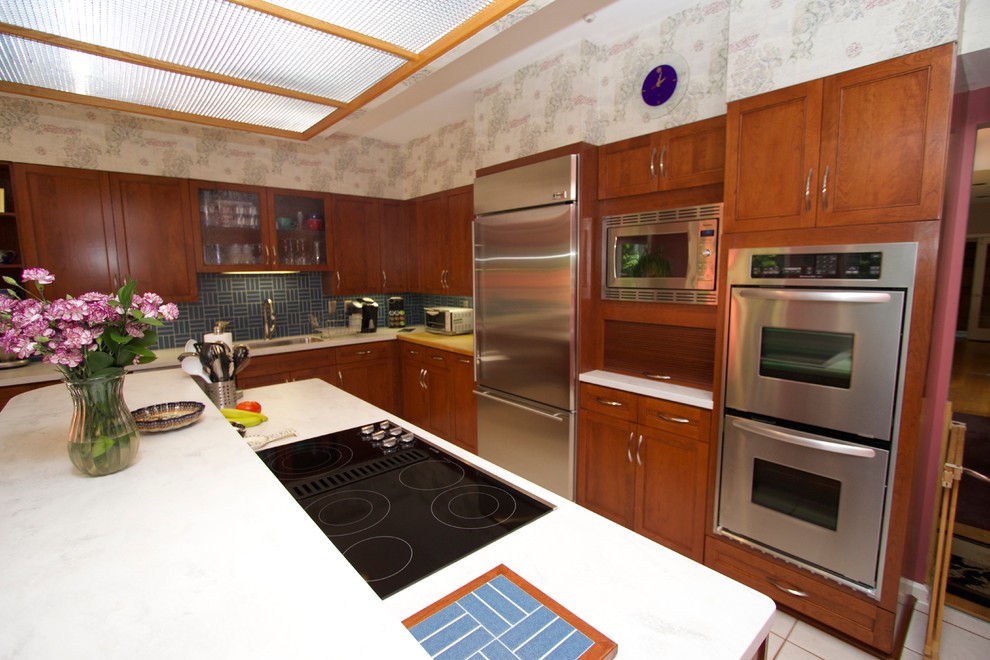 Transitional l-shaped ceramic tile open concept kitchen photo in Baltimore with an undermount sink, recessed-panel cabinets, medium tone wood cabinets, solid surface countertops, blue backsplash, ceramic backsplash, stainless steel appliances and an island
