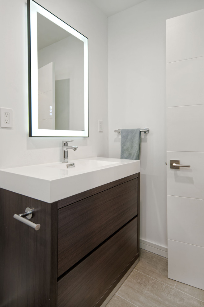 Inredning av ett modernt vit vitt badrum, med släta luckor, skåp i mörkt trä, en dusch i en alkov, en toalettstol med hel cisternkåpa, brun kakel, vita väggar, ett integrerad handfat, bänkskiva i akrylsten och med dusch som är öppen