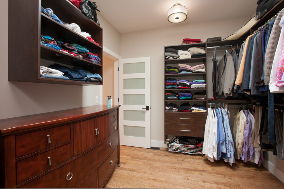 Mid-sized contemporary gender-neutral walk-in wardrobe in Vancouver with flat-panel cabinets, dark wood cabinets and medium hardwood floors.