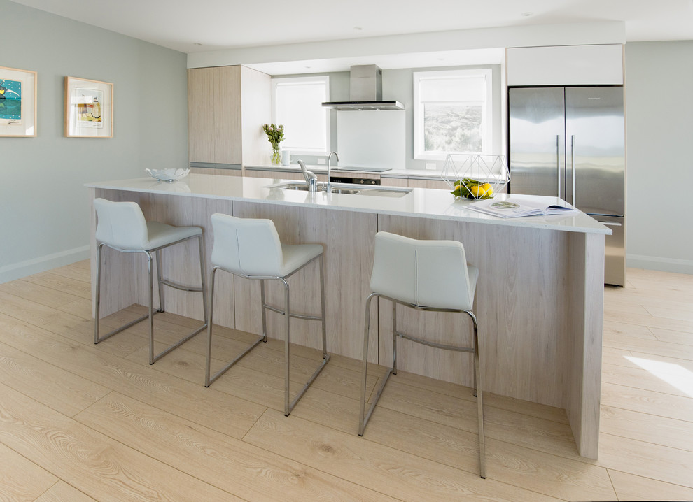 This is an example of a mid-sized scandinavian single-wall eat-in kitchen in Auckland with a double-bowl sink, light wood cabinets, quartz benchtops, white splashback, glass sheet splashback, stainless steel appliances, light hardwood floors and with island.
