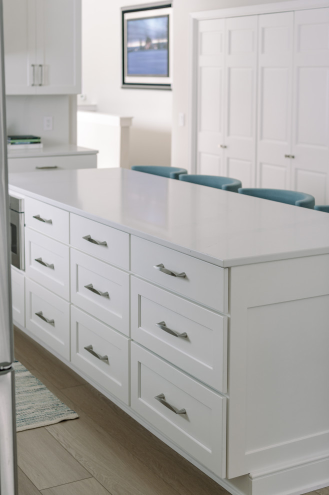 Inspiration for a large transitional l-shaped laminate floor and brown floor eat-in kitchen remodel with an undermount sink, shaker cabinets, white cabinets, quartz countertops, white backsplash, quartz backsplash, stainless steel appliances, an island and white countertops