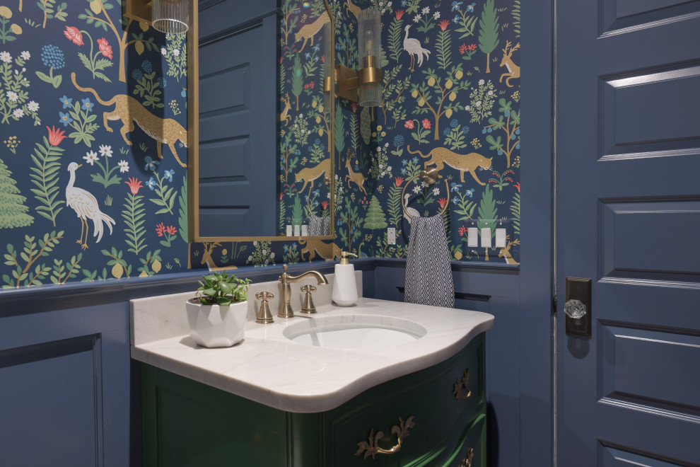 Inspiration for a mid-sized traditional powder room in DC Metro with furniture-like cabinets, green cabinets, blue walls, medium hardwood floors, an undermount sink, engineered quartz benchtops, brown floor, white benchtops, a freestanding vanity and wallpaper.