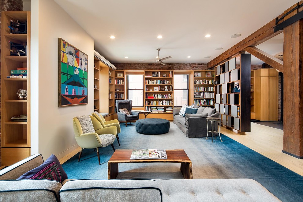 Industrial living room in New York with a library, white walls and light hardwood floors.