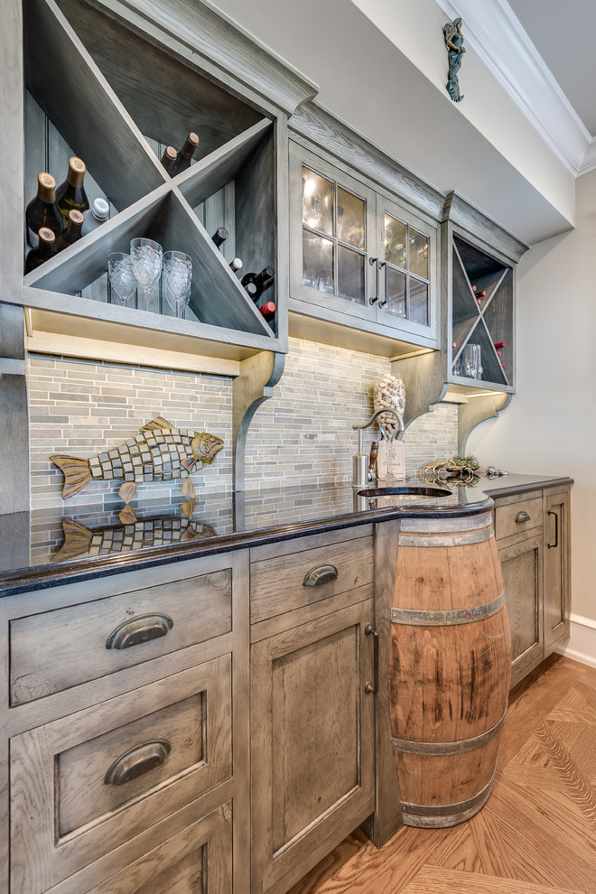 Inspiration for a mid-sized beach style single-wall wet bar in Philadelphia with a drop-in sink, grey cabinets, granite benchtops, black splashback, mosaic tile splashback and medium hardwood floors.
