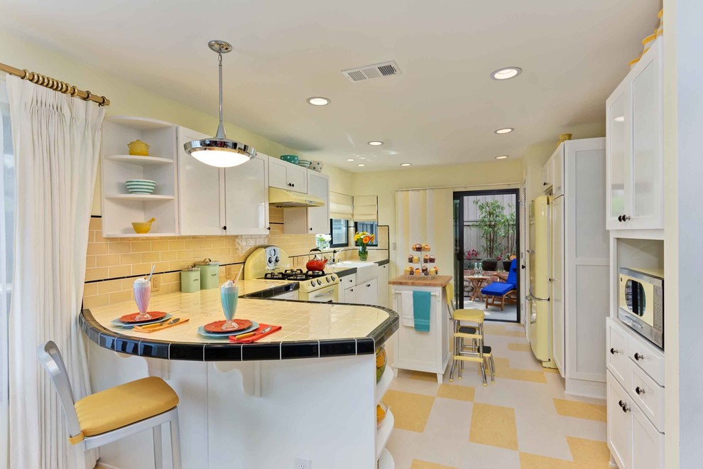 Inspiration for a traditional u-shaped separate kitchen in San Diego with a farmhouse sink, shaker cabinets, white cabinets, tile benchtops, yellow splashback, subway tile splashback, coloured appliances, multi-coloured floor and yellow benchtop.