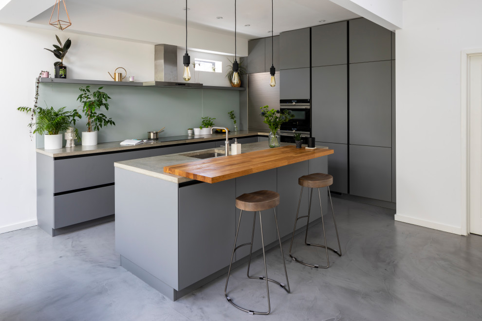 Contemporary u-shaped kitchen in London with an undermount sink, flat-panel cabinets, grey cabinets, concrete benchtops, blue splashback, glass sheet splashback, panelled appliances, with island, grey floor and grey benchtop.