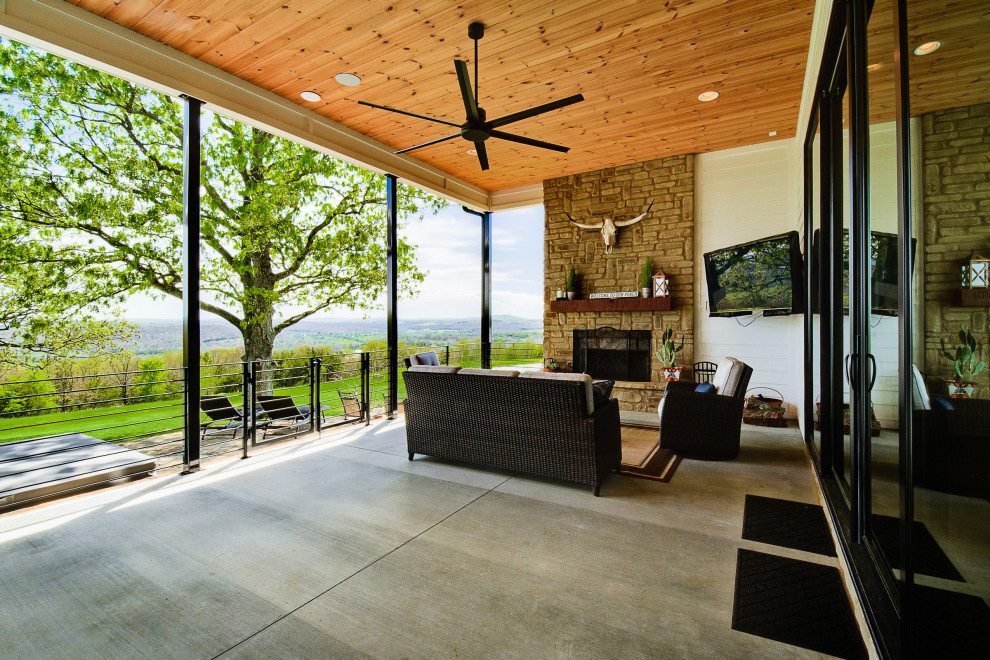 Immagine di un ampio patio o portico country dietro casa con un caminetto, lastre di cemento e un tetto a sbalzo