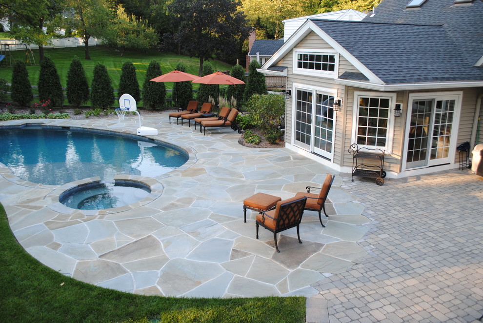 Photo of a large traditional backyard kidney-shaped pool in New York with a hot tub and natural stone pavers.