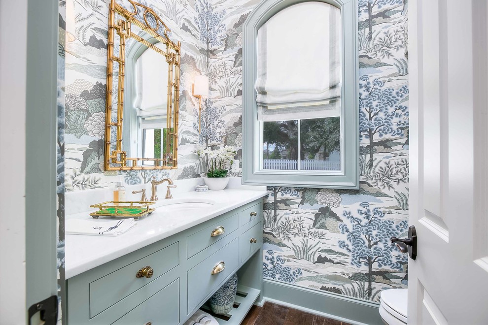 Inspiration for a mid-sized transitional bathroom in New Orleans with recessed-panel cabinets, turquoise cabinets, a one-piece toilet, multi-coloured walls, medium hardwood floors, an undermount sink, marble benchtops, brown floor, white benchtops, green tile, a single vanity, a built-in vanity and wallpaper.