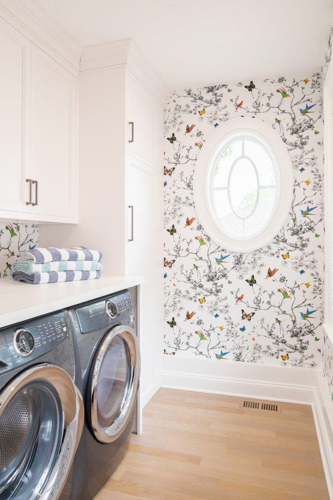 Large beach style single-wall light wood floor, beige floor and wallpaper dedicated laundry room photo in Bridgeport with raised-panel cabinets, white cabinets, a side-by-side washer/dryer and white countertops