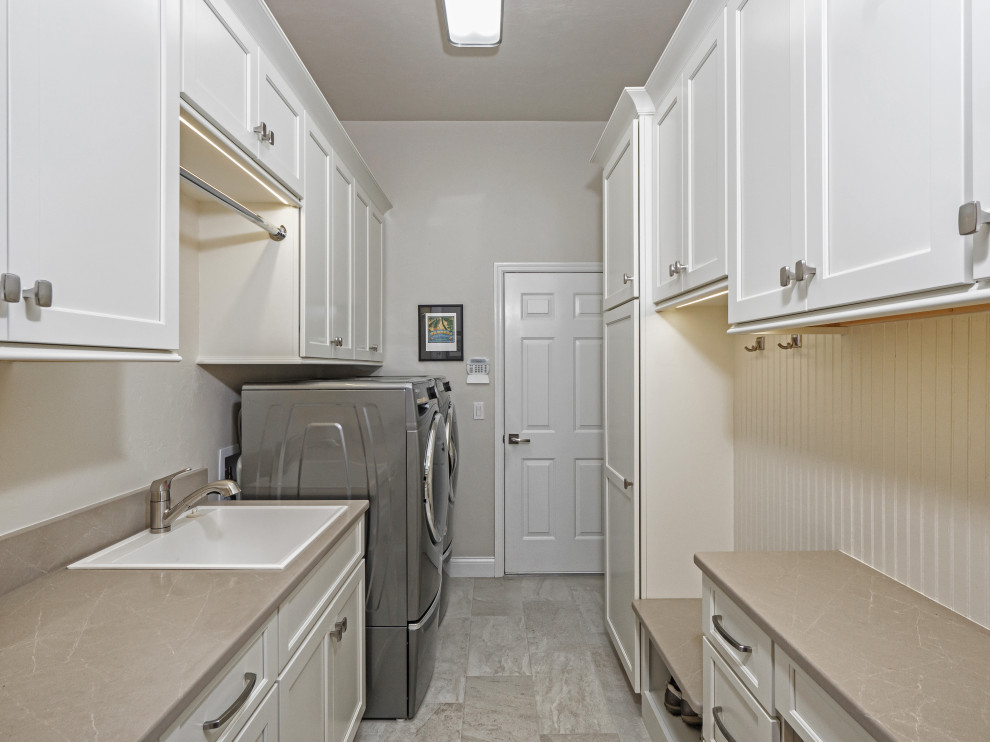 Photo of a mid-sized transitional galley utility room in Miami with a drop-in sink, recessed-panel cabinets, white cabinets, quartz benchtops, white splashback, shiplap splashback, beige walls, a side-by-side washer and dryer, grey floor and beige benchtop.