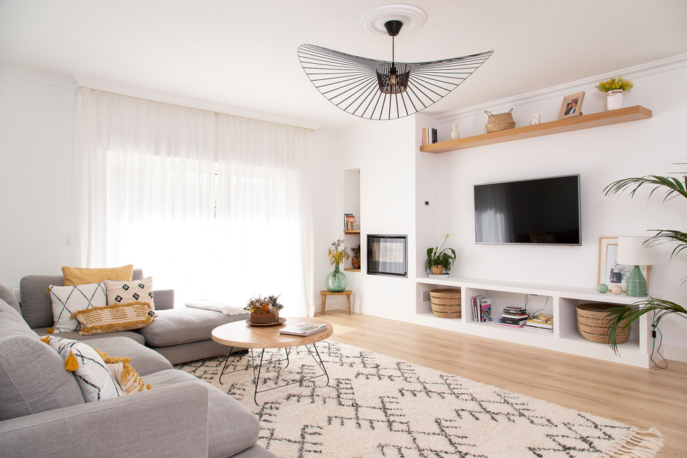 Photo of a large contemporary open concept living room in Madrid with white walls, light hardwood floors, a standard fireplace, a metal fireplace surround, a wall-mounted tv and beige floor.