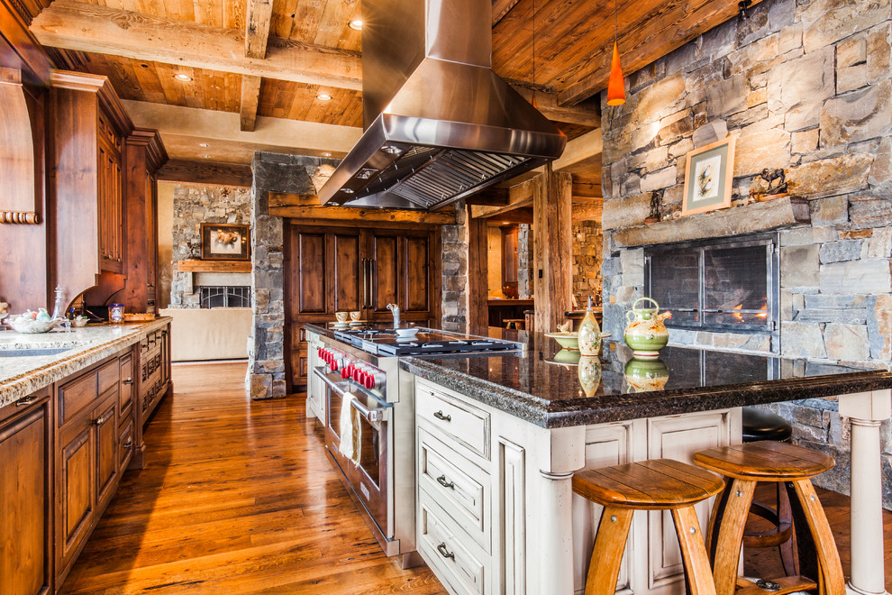 Example of a large mountain style single-wall dark wood floor eat-in kitchen design with an undermount sink, raised-panel cabinets, dark wood cabinets, granite countertops, stainless steel appliances and an island