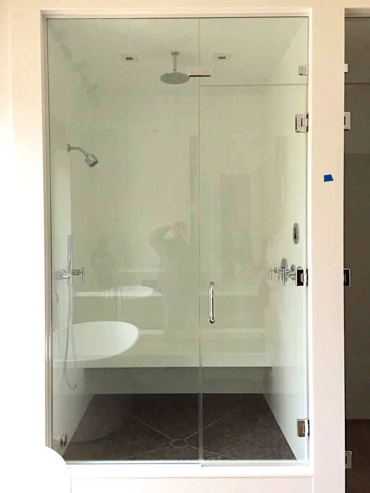This is an example of a modern master bathroom in Baltimore with glass-front cabinets, white cabinets, white tile, glass sheet wall, glass benchtops, a hinged shower door and white benchtops.