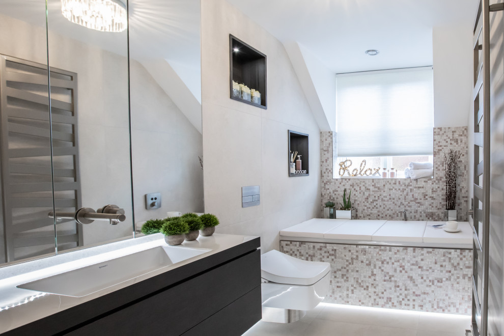 Cette image montre une salle de bain principale design en bois foncé de taille moyenne avec un placard à porte plane, une baignoire posée, WC suspendus, un carrelage beige, des carreaux de porcelaine et meuble-lavabo suspendu.