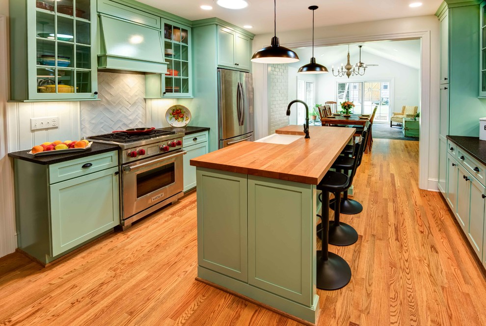 Photo of a small midcentury galley eat-in kitchen in Raleigh with a farmhouse sink, shaker cabinets, turquoise cabinets, granite benchtops, white splashback, porcelain splashback, stainless steel appliances, medium hardwood floors, with island, brown floor and black benchtop.