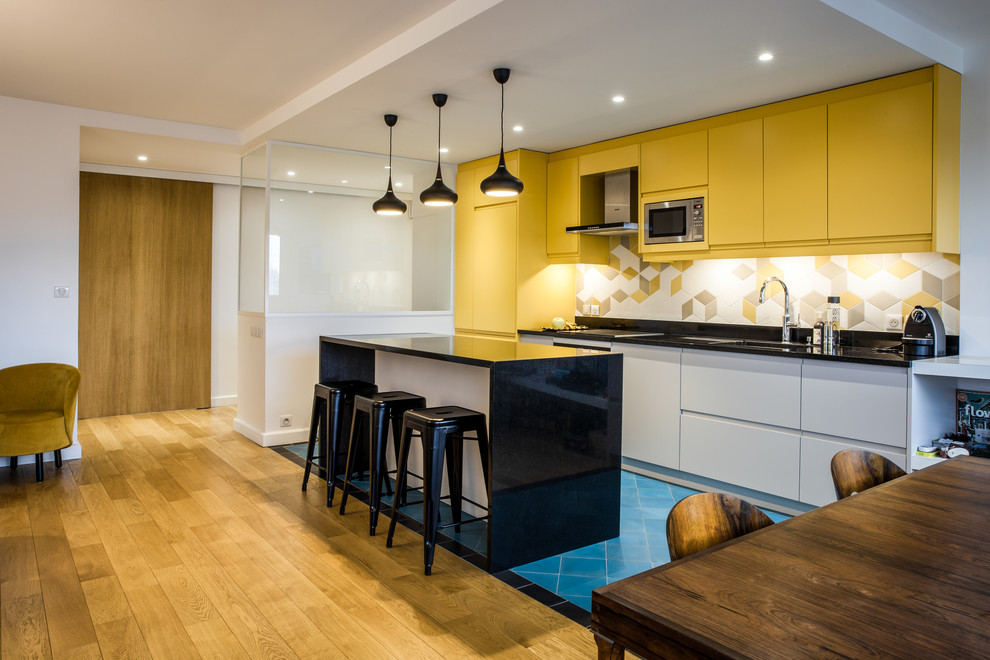 This is an example of a mid-sized scandinavian single-wall eat-in kitchen in Paris with a double-bowl sink, yellow cabinets, yellow splashback, porcelain splashback, stainless steel appliances, ceramic floors, with island, blue floor and black benchtop.