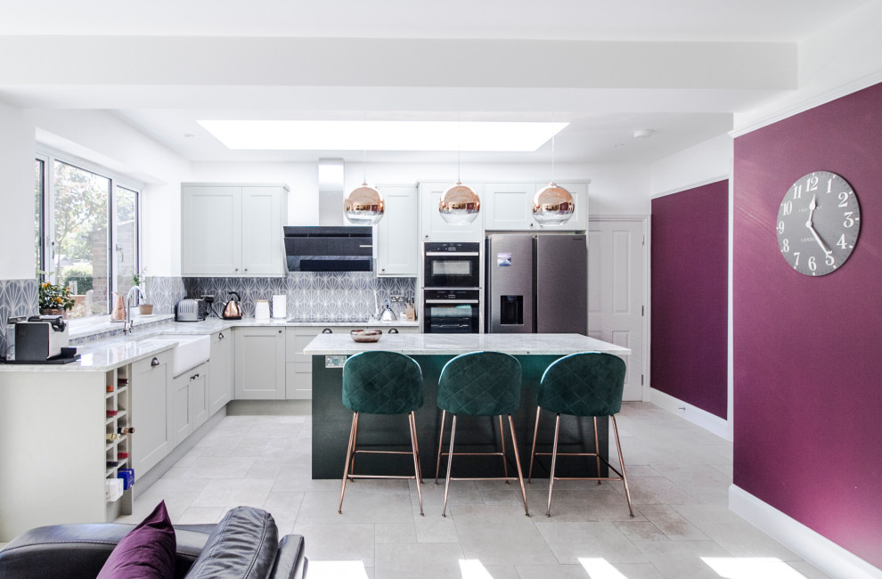 Photo of a mid-sized transitional l-shaped open plan kitchen in London with a farmhouse sink, shaker cabinets, granite benchtops, blue splashback, ceramic splashback, stainless steel appliances, limestone floors, with island, grey floor and white benchtop.