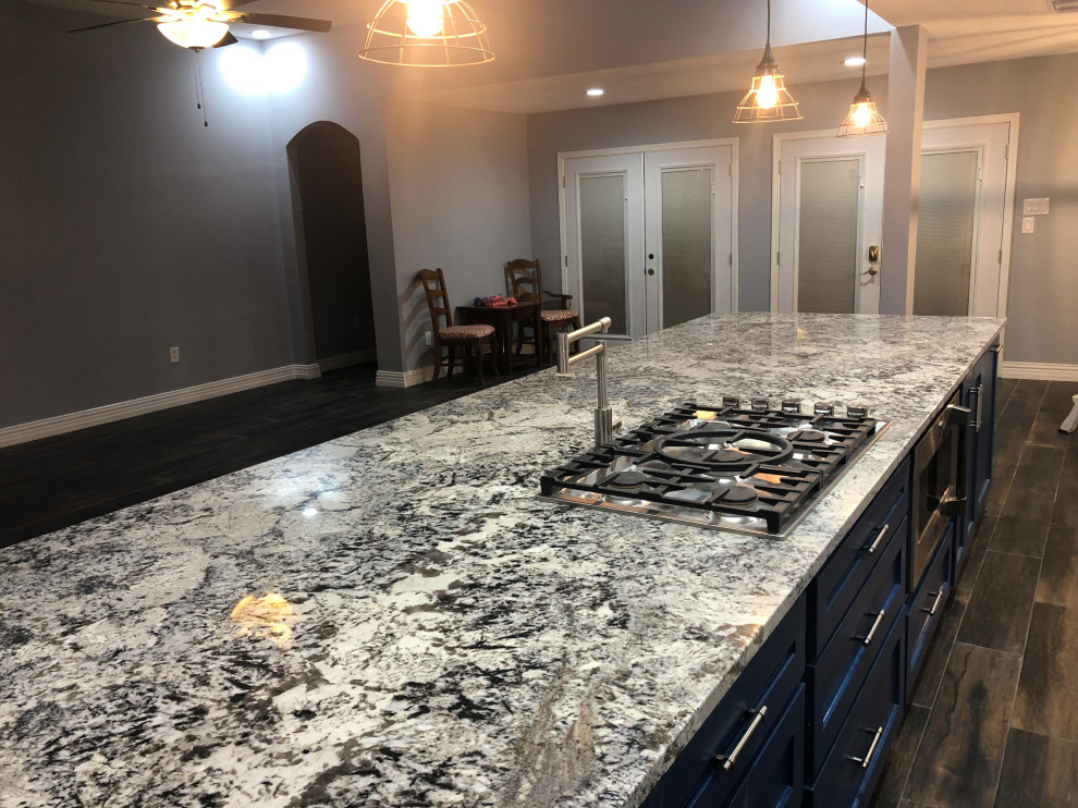 Expansive contemporary kitchen in Houston with a farmhouse sink, shaker cabinets, blue cabinets, granite benchtops, white splashback, travertine splashback, stainless steel appliances, light hardwood floors, with island, brown floor and blue benchtop.