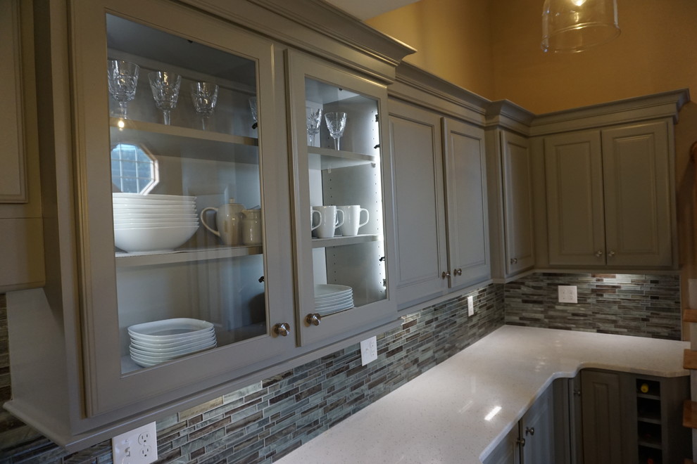 Inspiration for a small timeless l-shaped medium tone wood floor eat-in kitchen remodel in Providence with a triple-bowl sink, raised-panel cabinets, gray cabinets, quartz countertops, gray backsplash, mosaic tile backsplash, stainless steel appliances, an island and white countertops