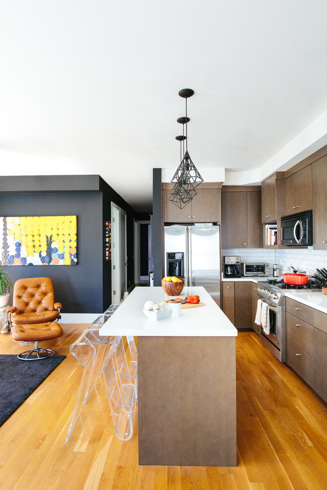 This is an example of a contemporary l-shaped open plan kitchen in San Francisco with flat-panel cabinets, dark wood cabinets, white splashback, subway tile splashback, stainless steel appliances, medium hardwood floors, with island, an undermount sink and quartz benchtops.
