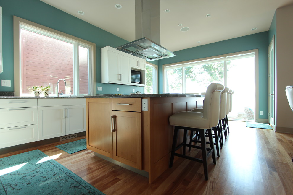 This is an example of a mid-sized transitional l-shaped open plan kitchen in Other with an undermount sink, shaker cabinets, light wood cabinets, quartz benchtops, metallic splashback, panelled appliances, light hardwood floors and with island.
