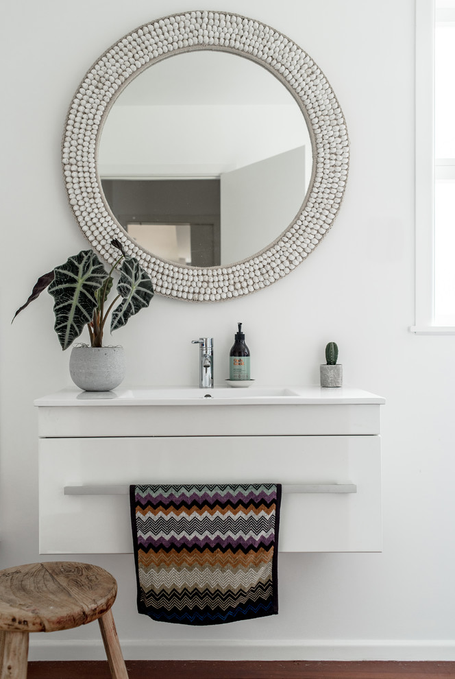 Photo of a mid-sized contemporary bathroom in Auckland with white cabinets, white walls, medium hardwood floors, a drop-in sink, solid surface benchtops and brown floor.