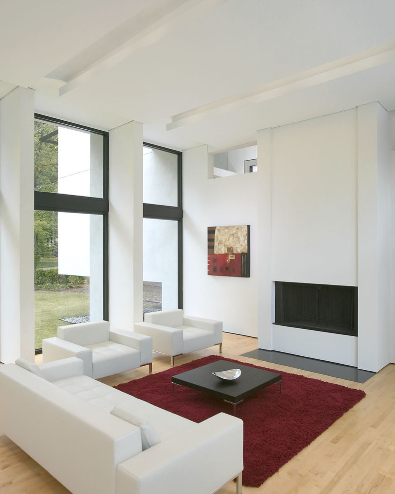 This is an example of a mid-sized modern formal open concept living room in Atlanta with white walls, light hardwood floors, a standard fireplace, a plaster fireplace surround and a concealed tv.