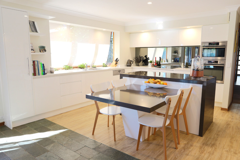 Photo of a mid-sized contemporary galley eat-in kitchen in Sydney with a double-bowl sink, flat-panel cabinets, white cabinets, quartz benchtops, grey splashback, mirror splashback, stainless steel appliances, light hardwood floors, with island, white floor and white benchtop.