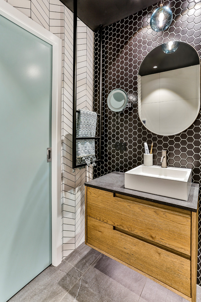 Small industrial master bathroom in Auckland with furniture-like cabinets, medium wood cabinets, a curbless shower, a wall-mount toilet, black and white tile, ceramic tile, black walls, porcelain floors, a vessel sink, engineered quartz benchtops, grey floor, an open shower and grey benchtops.