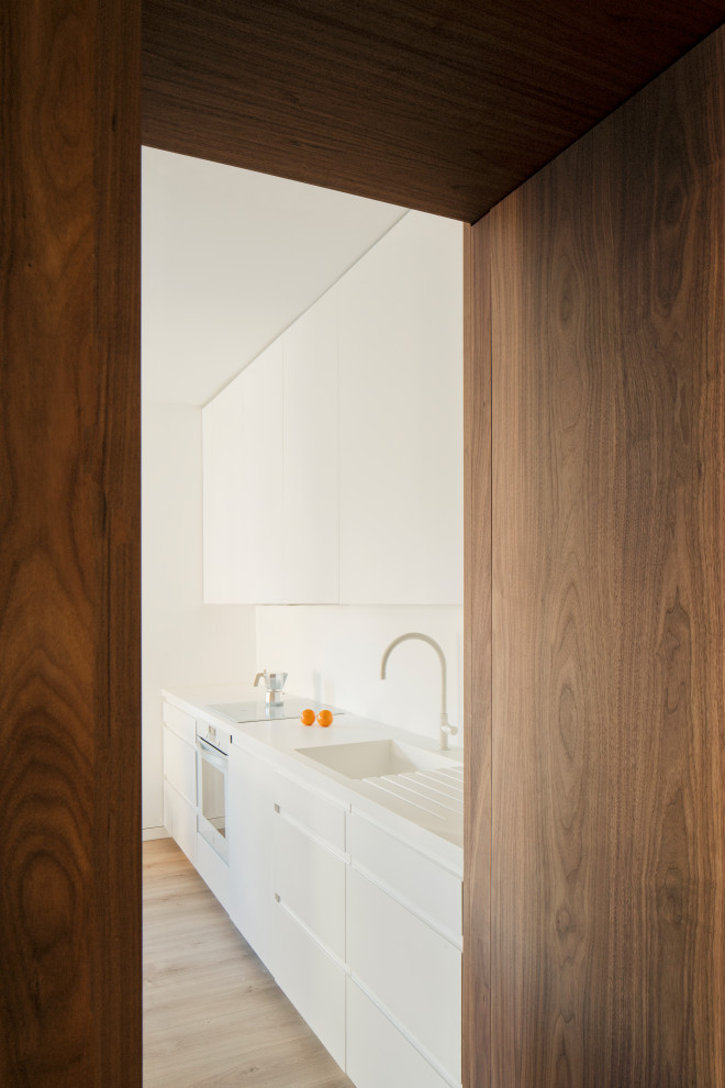 This is an example of a small scandinavian open plan kitchen in Madrid with an integrated sink, flat-panel cabinets, white cabinets, quartz benchtops, white splashback, engineered quartz splashback, white appliances, medium hardwood floors, with island, brown floor, white benchtop and recessed.