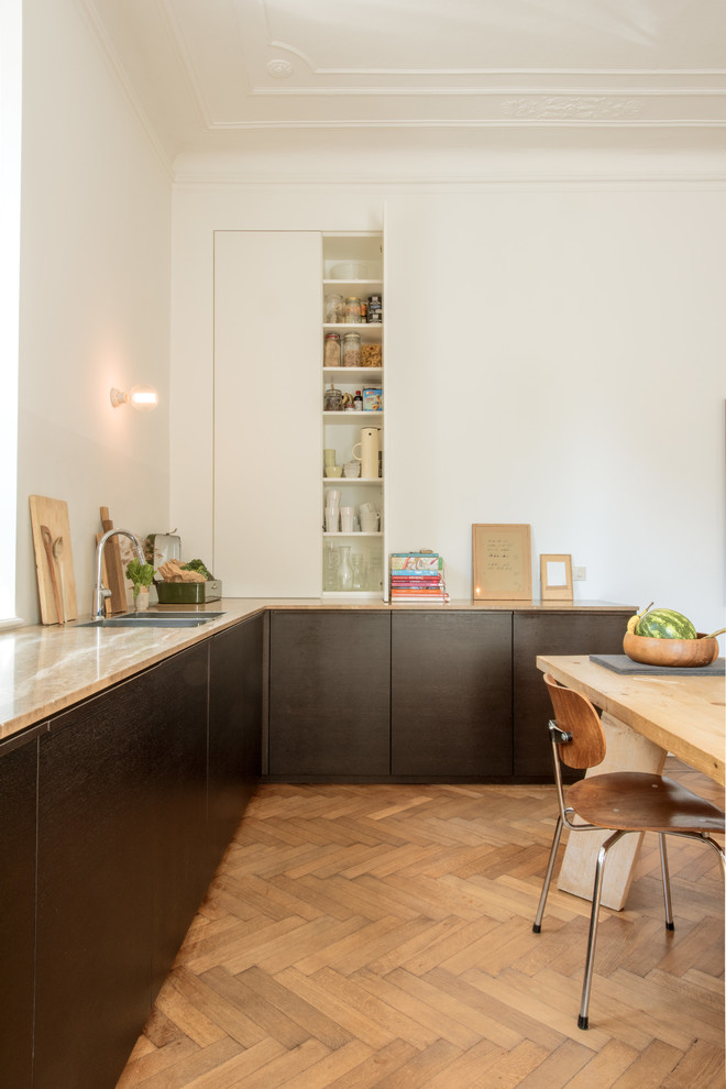 Photo of a scandinavian l-shaped eat-in kitchen in Milan with a double-bowl sink, flat-panel cabinets, black cabinets, white splashback, medium hardwood floors, brown floor and brown benchtop.