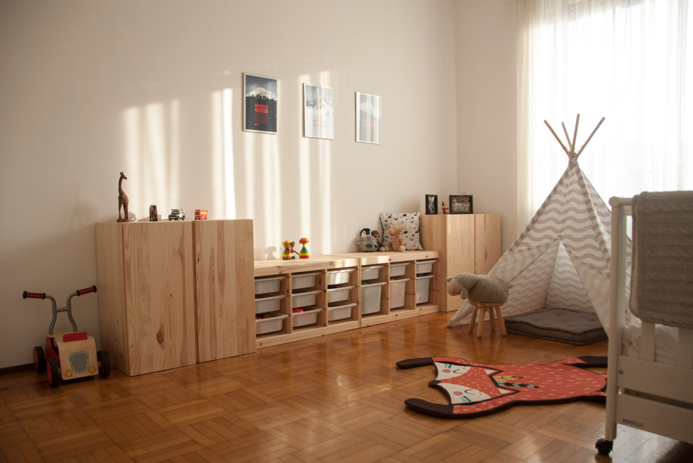 Photo of a mid-sized scandinavian gender-neutral nursery in Milan with white walls, light hardwood floors and brown floor.
