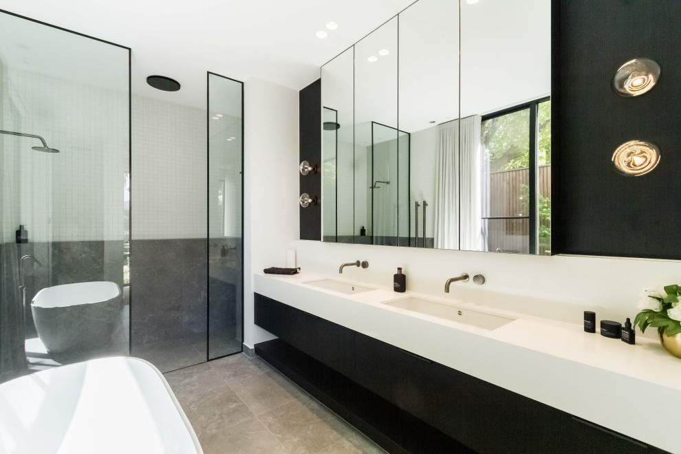 Inspiration for a large contemporary master bathroom in Melbourne with flat-panel cabinets, black cabinets, a freestanding tub, white tile, gray tile, ceramic tile, white walls, ceramic floors, an undermount sink, engineered quartz benchtops, white benchtops, grey floor and an alcove shower.