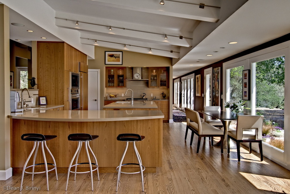 Photo of a large eclectic galley eat-in kitchen in San Francisco with stainless steel appliances, an undermount sink, flat-panel cabinets, medium wood cabinets, solid surface benchtops, light hardwood floors and a peninsula.