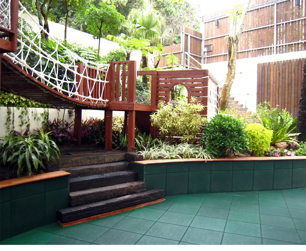 Large tropical backyard shaded formal garden in Hong Kong with with outdoor playset and mulch for spring.