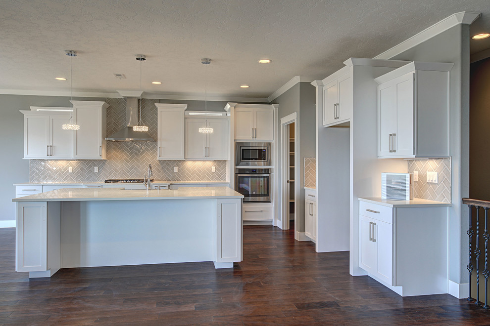 Open concept kitchen - mid-sized transitional l-shaped medium tone wood floor open concept kitchen idea in Seattle with an undermount sink, shaker cabinets, white cabinets, quartz countertops, gray backsplash, glass tile backsplash, stainless steel appliances and an island