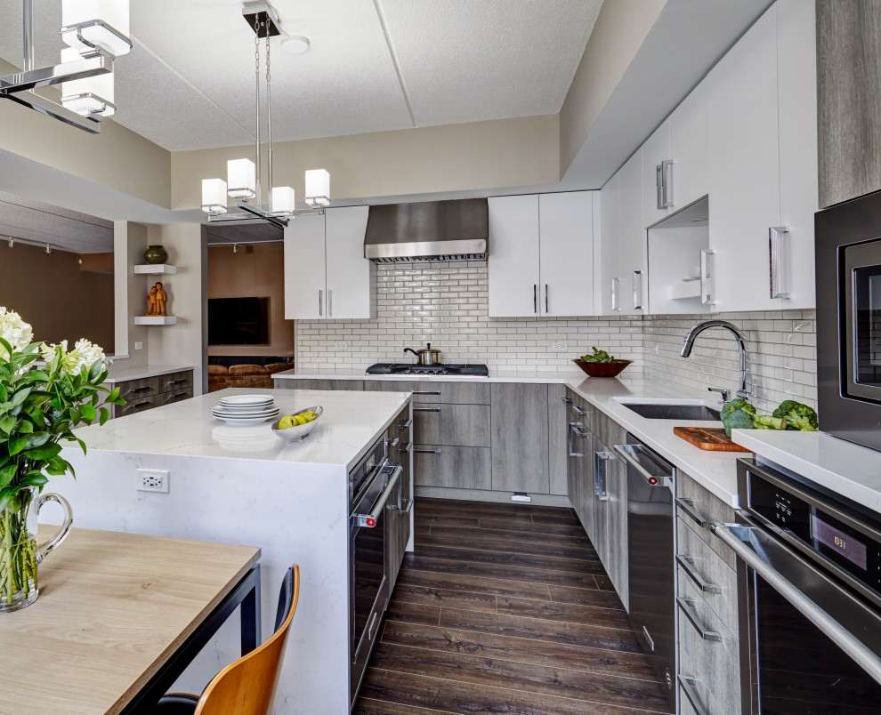 This is an example of a large contemporary l-shaped eat-in kitchen in Chicago with an undermount sink, flat-panel cabinets, quartz benchtops, white splashback, subway tile splashback, stainless steel appliances, porcelain floors, with island, grey floor, white benchtop and white cabinets.