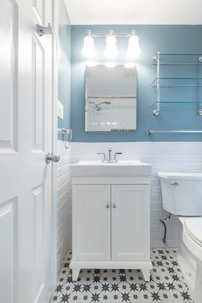 Photo of a small farmhouse ensuite bathroom in DC Metro with shaker cabinets, white cabinets, a submerged bath, a shower/bath combination, a one-piece toilet, white tiles, ceramic tiles, blue walls, ceramic flooring, an integrated sink, solid surface worktops, multi-coloured floors, a shower curtain, white worktops, a wall niche, a single sink and a freestanding vanity unit.