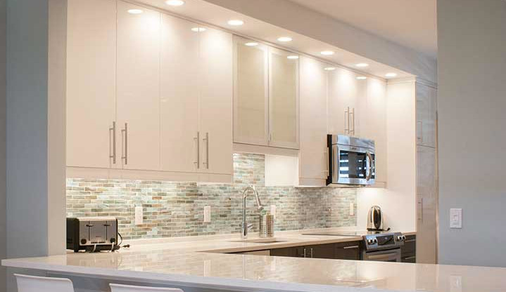 This is an example of a mid-sized modern l-shaped open plan kitchen in Tampa with an undermount sink, shaker cabinets, white cabinets, quartz benchtops, multi-coloured splashback, matchstick tile splashback, stainless steel appliances, medium hardwood floors, a peninsula and brown floor.