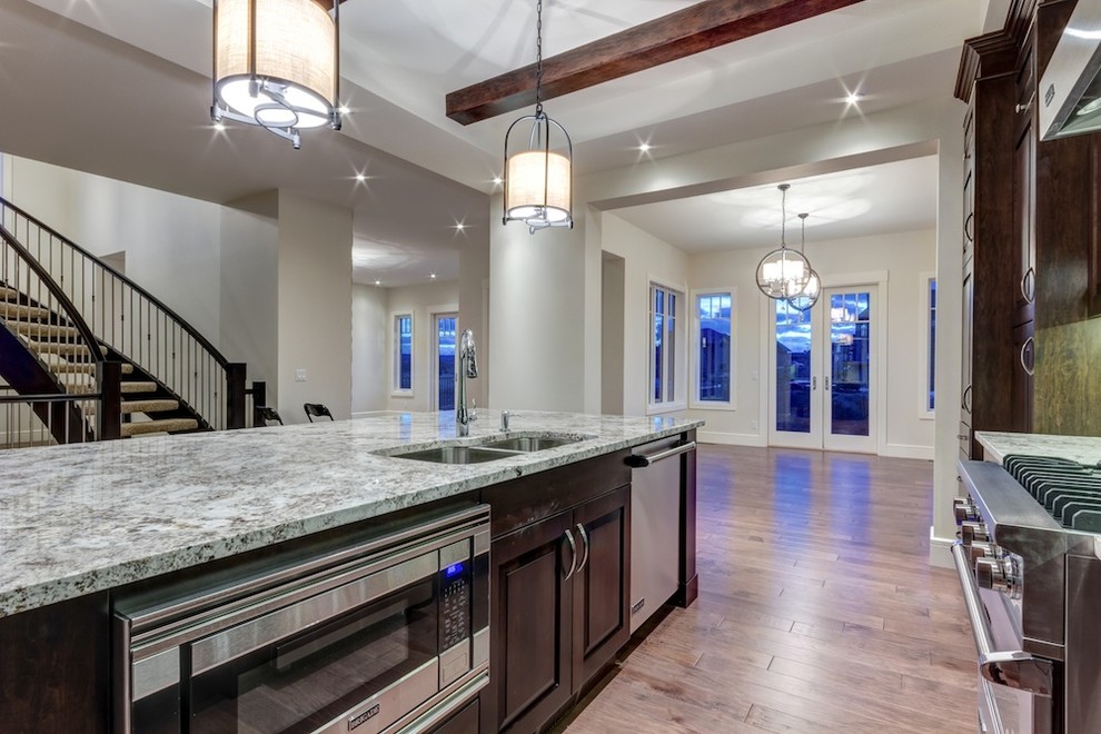 Transitional medium tone wood floor eat-in kitchen photo in Calgary with a double-bowl sink, raised-panel cabinets, dark wood cabinets, granite countertops, stainless steel appliances and an island
