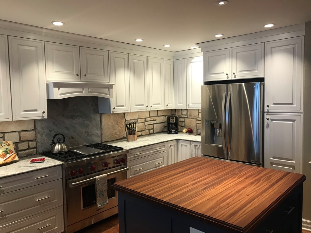 Expansive country l-shaped eat-in kitchen in New York with an undermount sink, raised-panel cabinets, white cabinets, granite benchtops, brown splashback, stone tile splashback, stainless steel appliances, medium hardwood floors, with island, brown floor and grey benchtop.