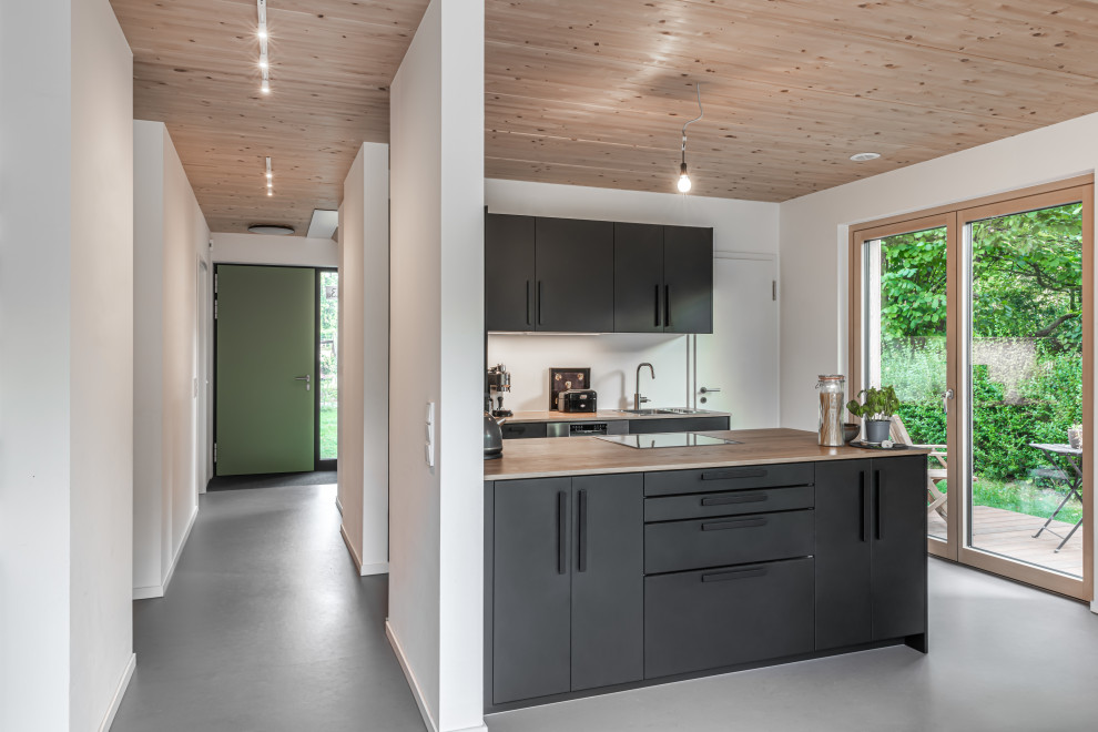 Modern u-shaped open plan kitchen in Essen with a double-bowl sink, flat-panel cabinets, black cabinets, wood benchtops, white splashback, linoleum floors, with island, pink floor, brown benchtop and wood.