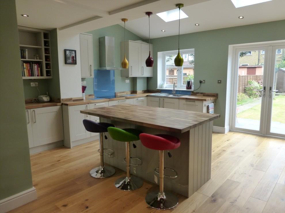 This is an example of a mid-sized contemporary galley eat-in kitchen in London with shaker cabinets, green cabinets, wood benchtops and with island.